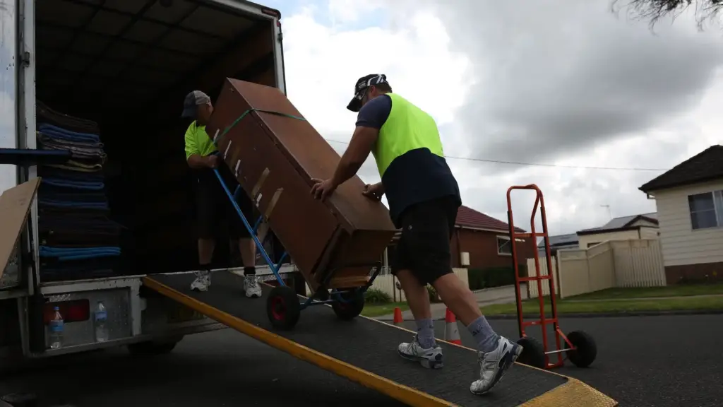 Two people in high-visibility clothing loading furniture into a van.